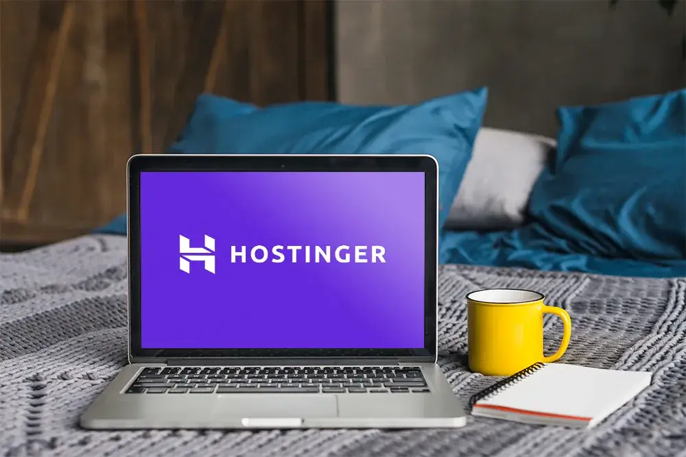 لابتوب يعرض شعار Hostinger بجانب كوب قهوة ودفتر